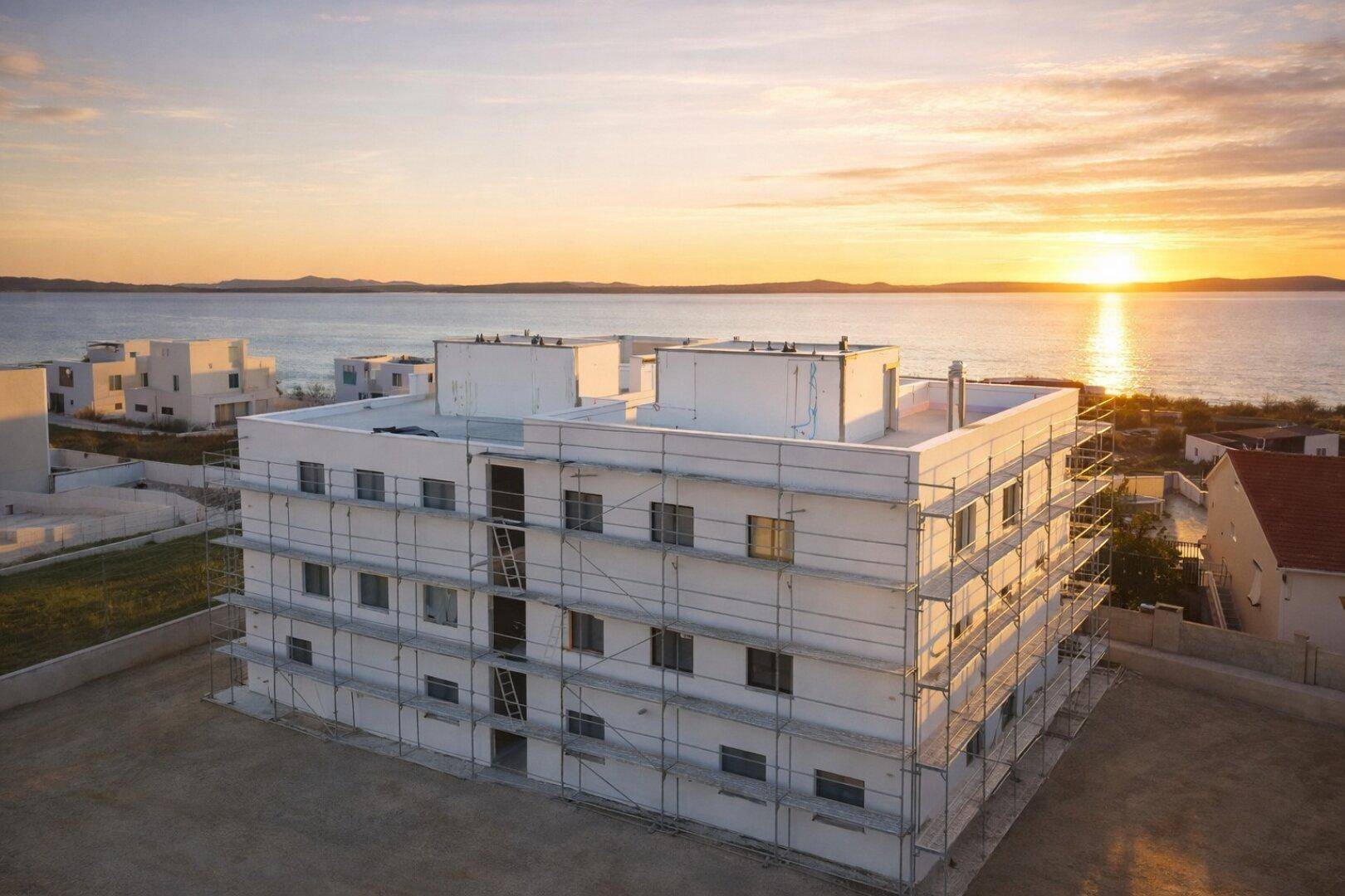 Neubau eines Apartmentgebäudes mit Gerüst und Meerblick bei Sonnenuntergang.