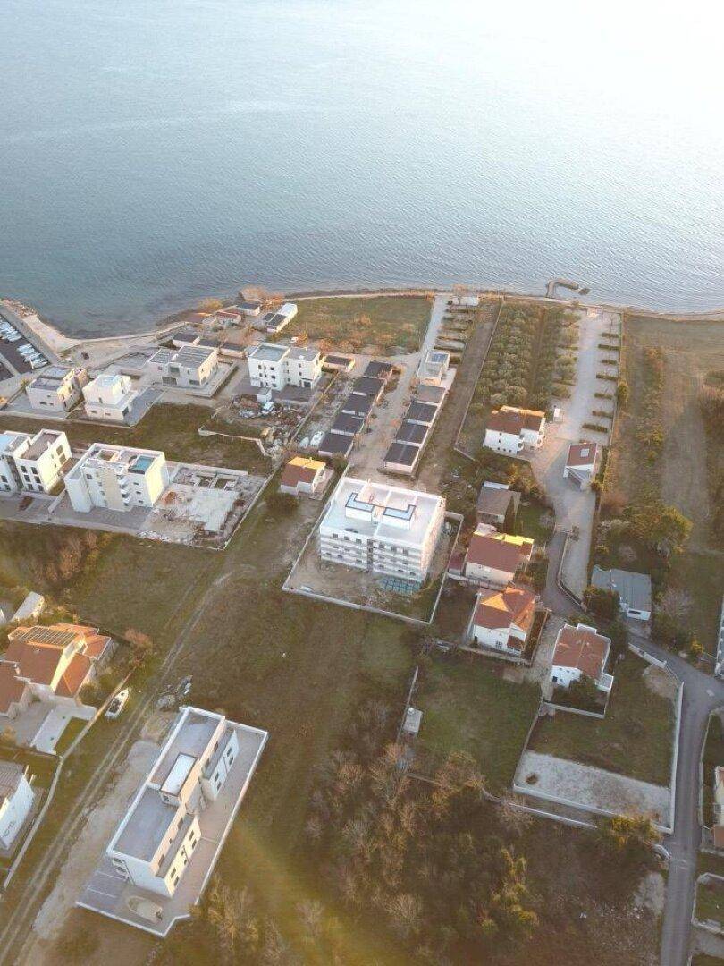 Luftaufnahme einer Küstenregion mit Wohngebäuden und dem Meer bei hellem Tageslicht.