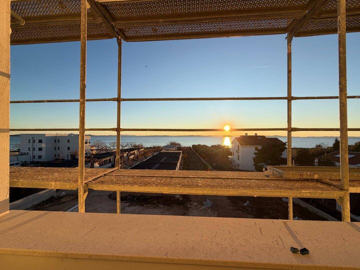 Blick durch ein Gerüst auf das Meer und den Sonnenuntergang von einem im Bau befindlichen Gebäude.