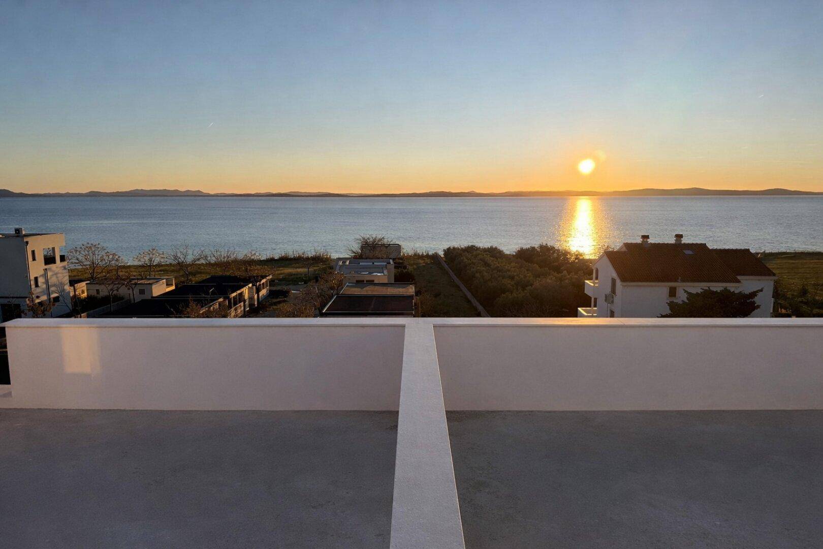Dachterrasse mit weitem Blick auf das Meer und den Sonnenuntergang am Horizont.