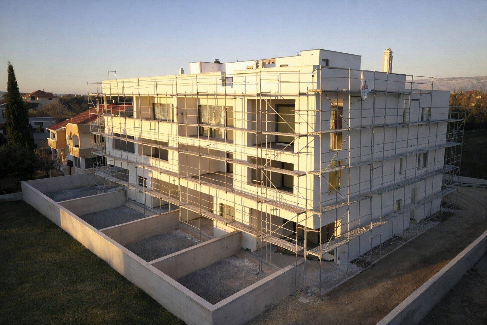 Neubau einer Wohnanlage mit Gerüst, umgeben von einer vorbereiteten Außenfläche.