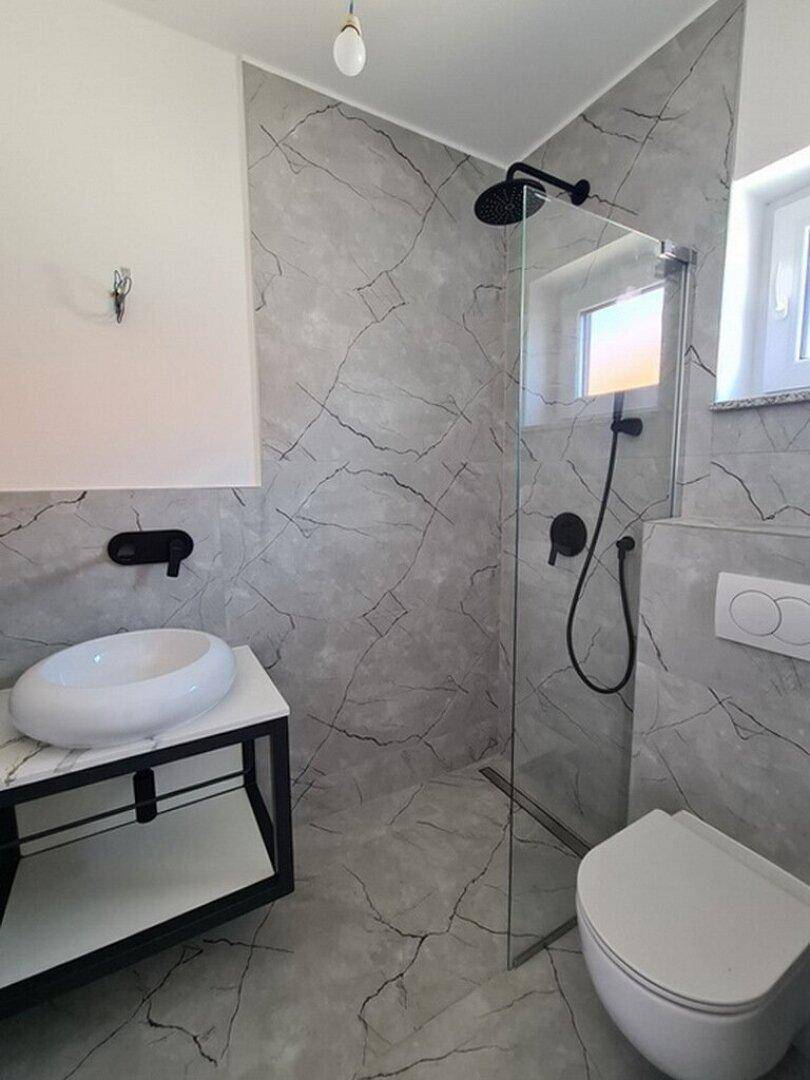 Modernes Badezimmer mit grauen Marmorfliesen, ebenerdiger Dusche und stilvollem Aufsatzwaschbecken.