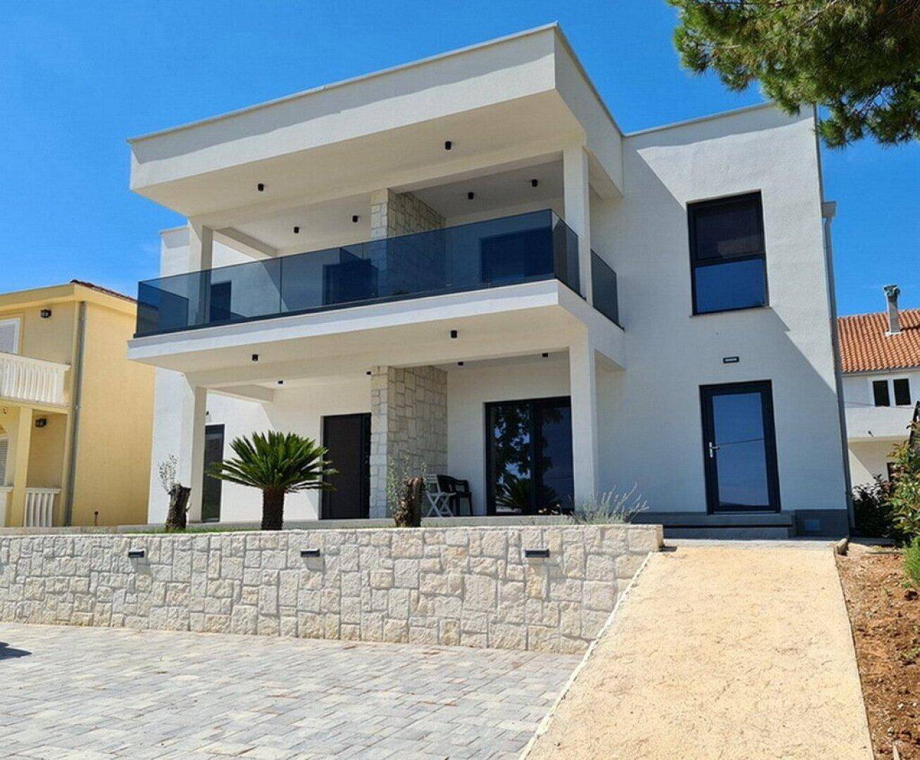 Elegante weiße Villa mit mehreren Balkonen, Steinverkleidung und moderner Architektur.