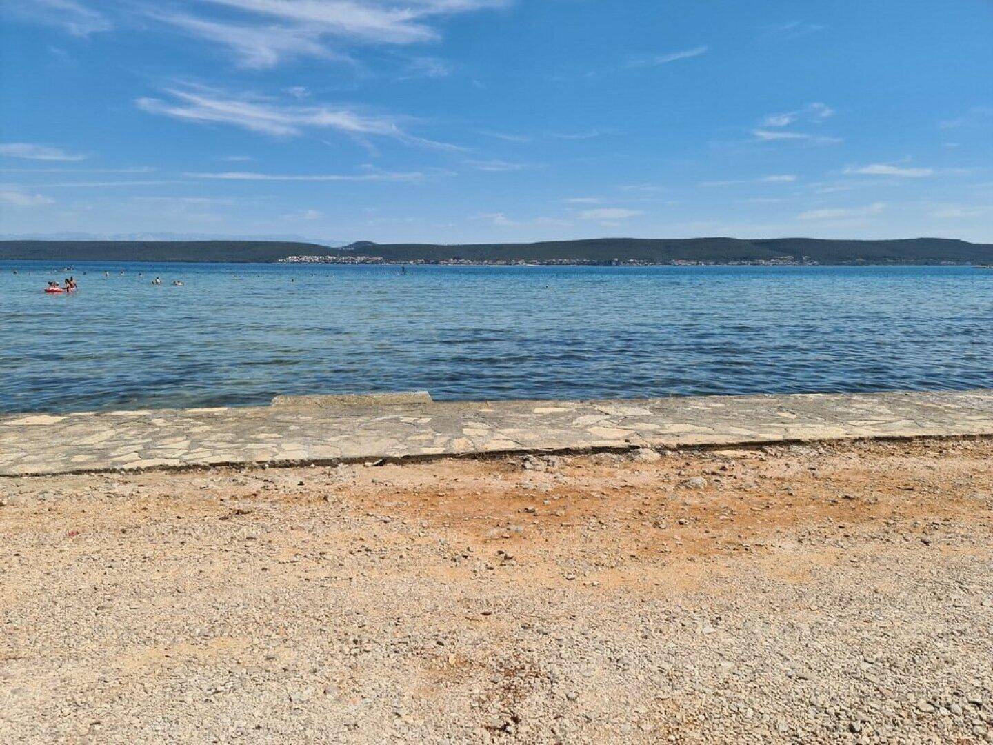 Weitläufiger Blick auf das ruhige blaue Meer und die ferne Küstenlinie unter einem klaren Himmel.