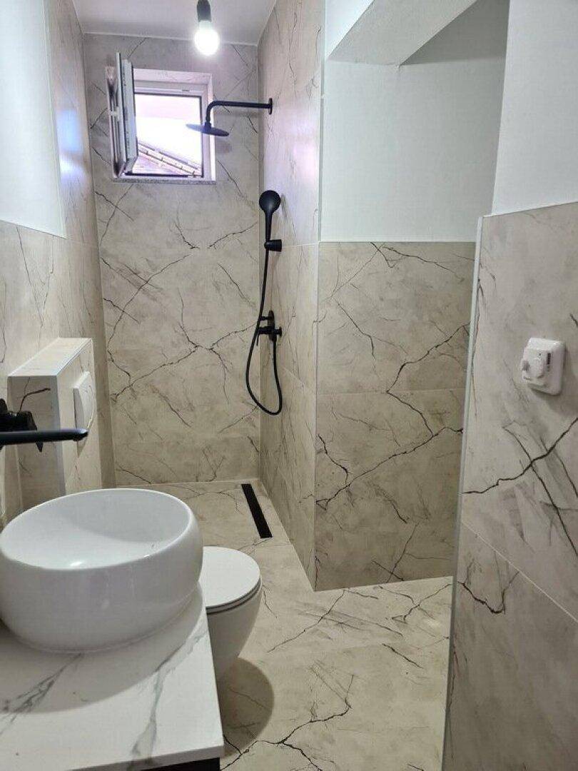 Modernes Badezimmer mit hellen Marmorfliesen, Dusche, Aufsatzwaschbecken und wandhängendem WC.