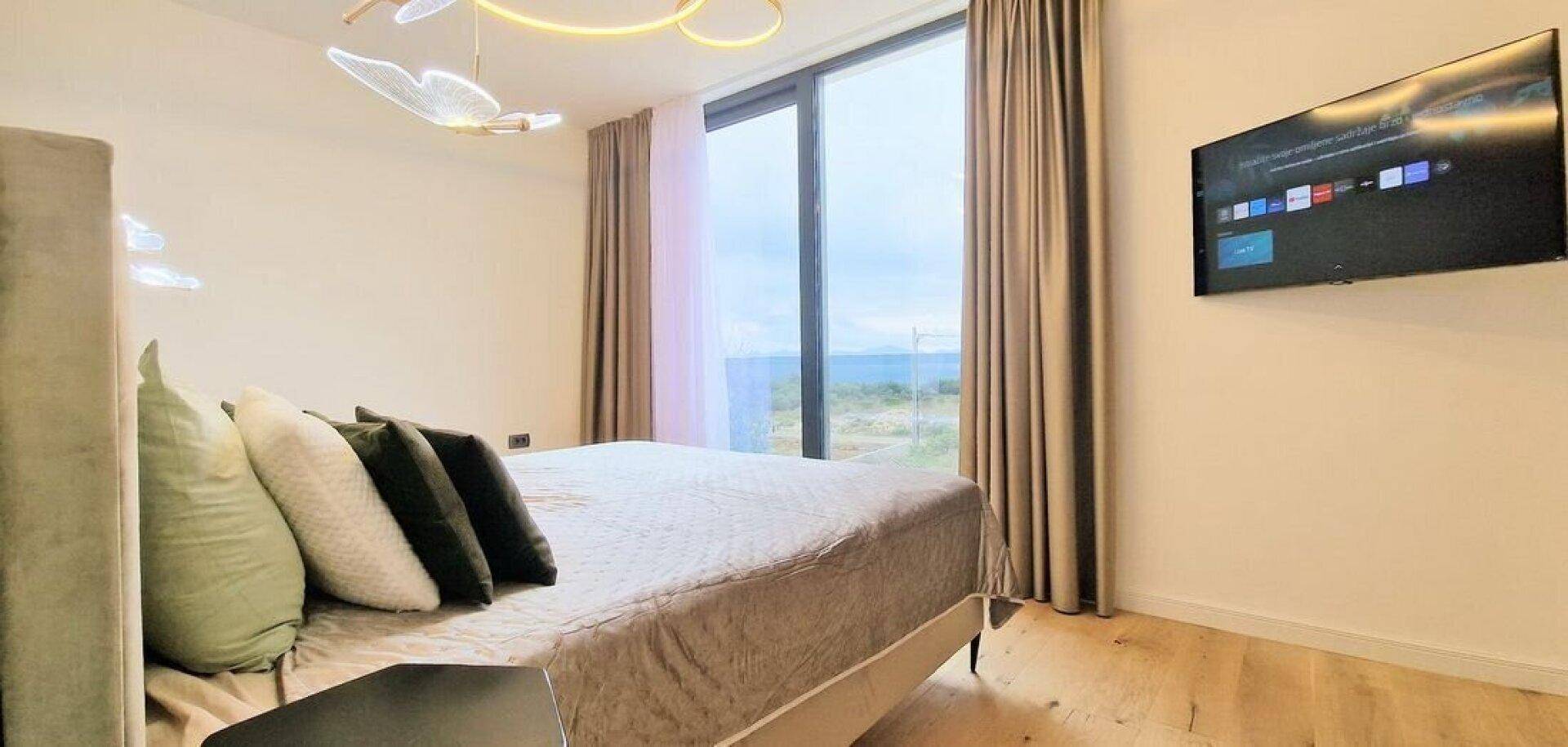 Helles Schlafzimmer mit großem Bett, bodentiefen Fenstern und Blick auf die Landschaft.