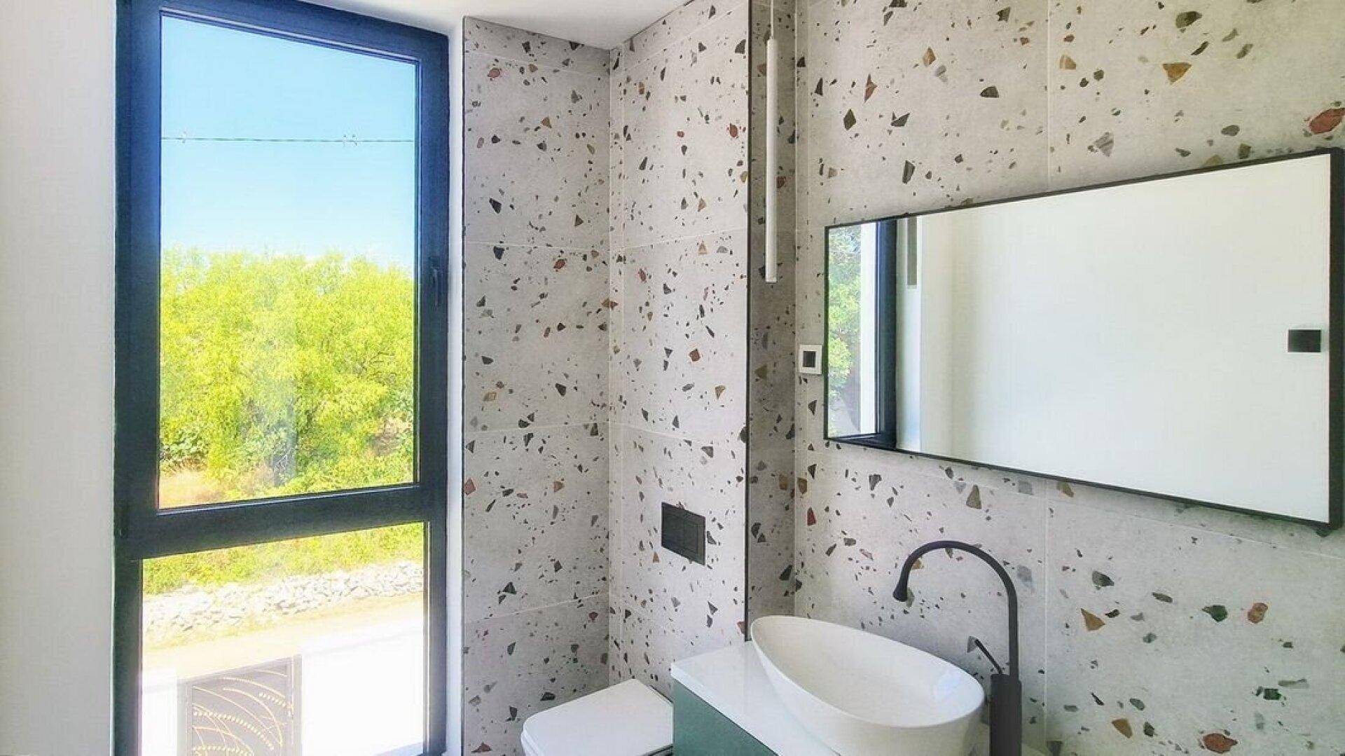 Modernes Badezimmer mit Terrazzo-Fliesen, stilvollem Waschbecken und großem Fenster.