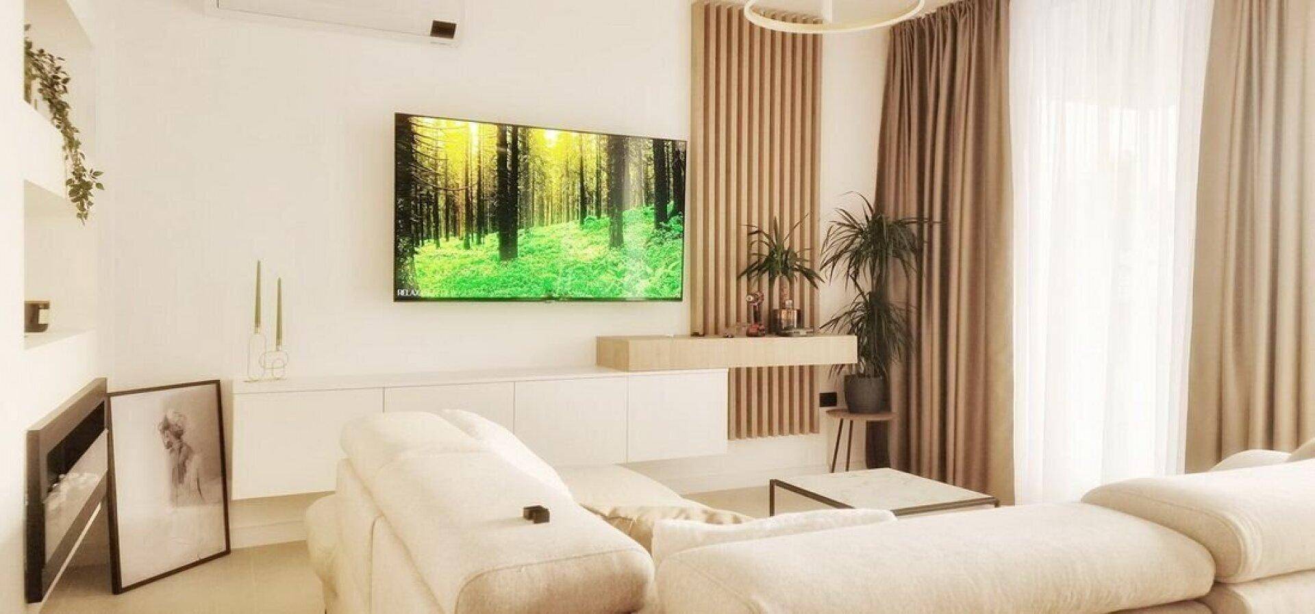 Detailansicht des modernen Wohnzimmers mit Wandfernseher, minimalistischer Einrichtung und Vorhängen.