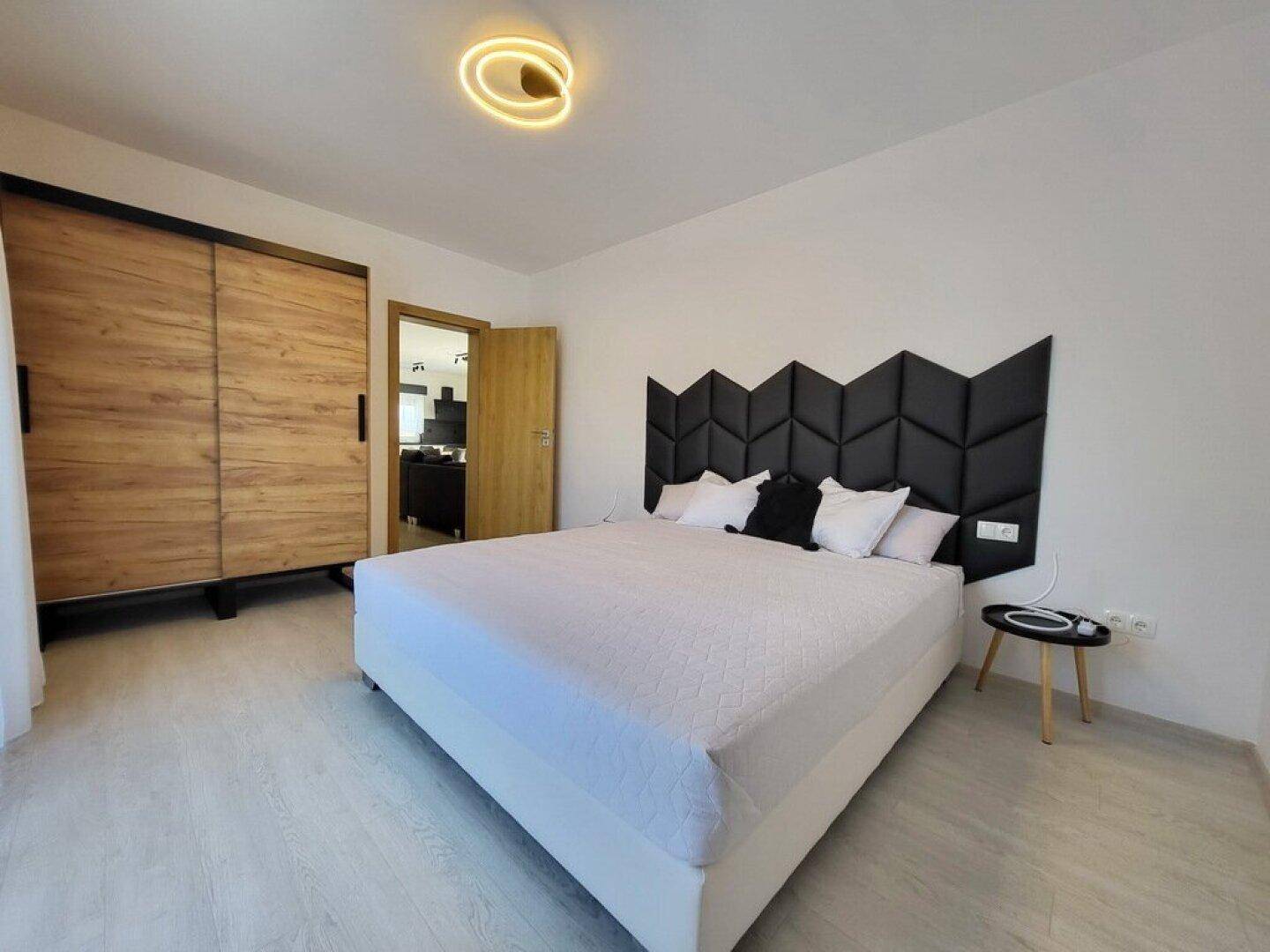 Modernes Schlafzimmer mit großem Bett, Holzkleiderschrank und minimalistischer Deckenleuchte.