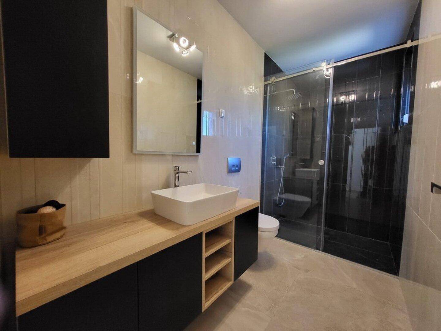 Modernes Badezimmer mit Einzelwaschbecken, Holzunterschrank und Duschkabine.