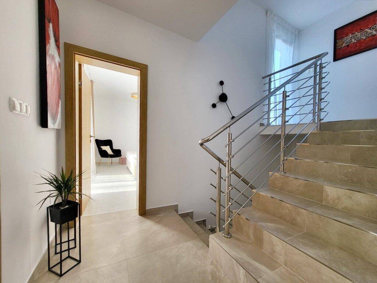 Heller Flur mit moderner Treppe, Edelstahlgeländer und Zugang zu weiteren Räumen.