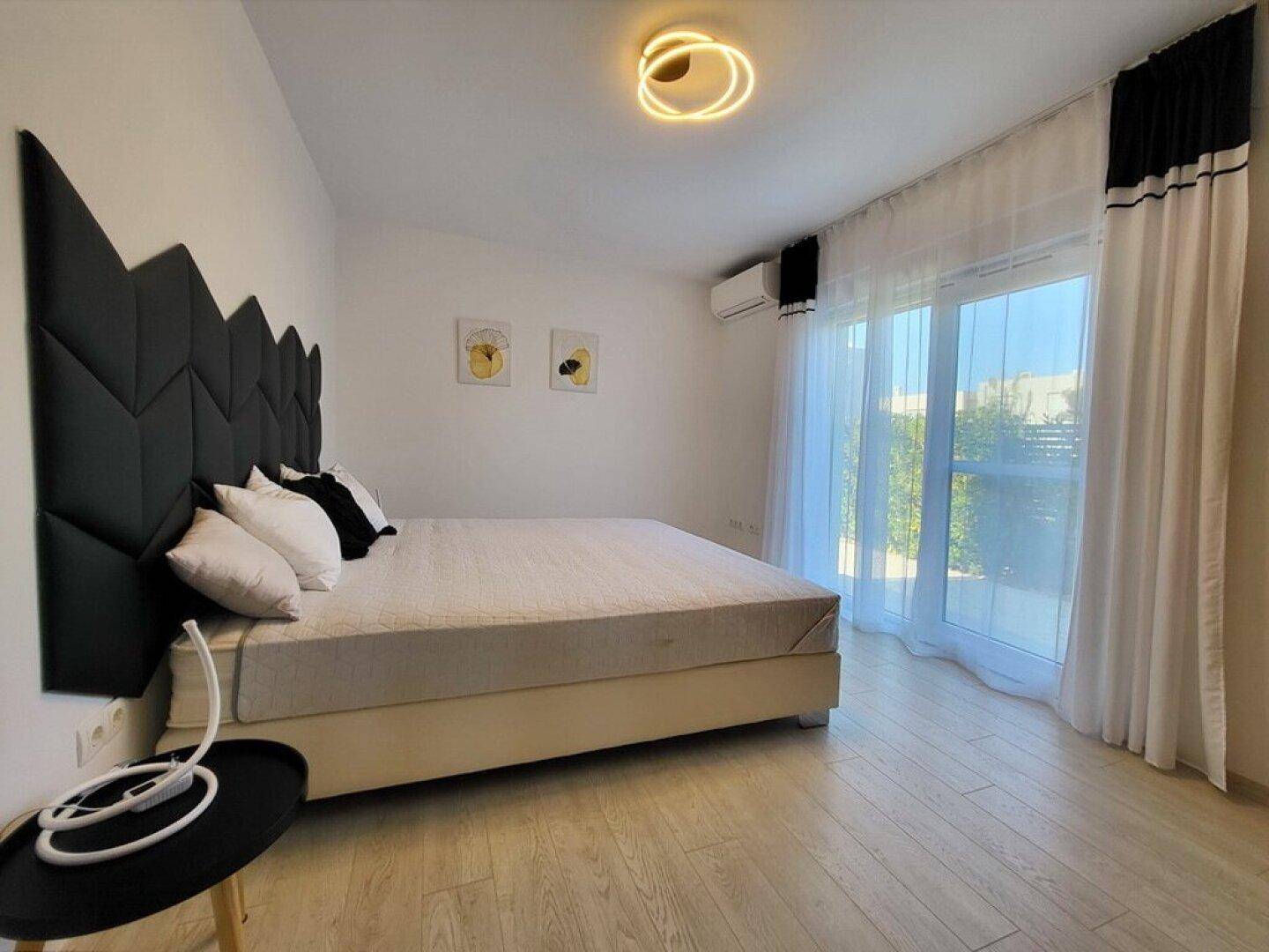 Helles Schlafzimmer mit großen Glasfenstern, die viel Tageslicht hereinlassen.