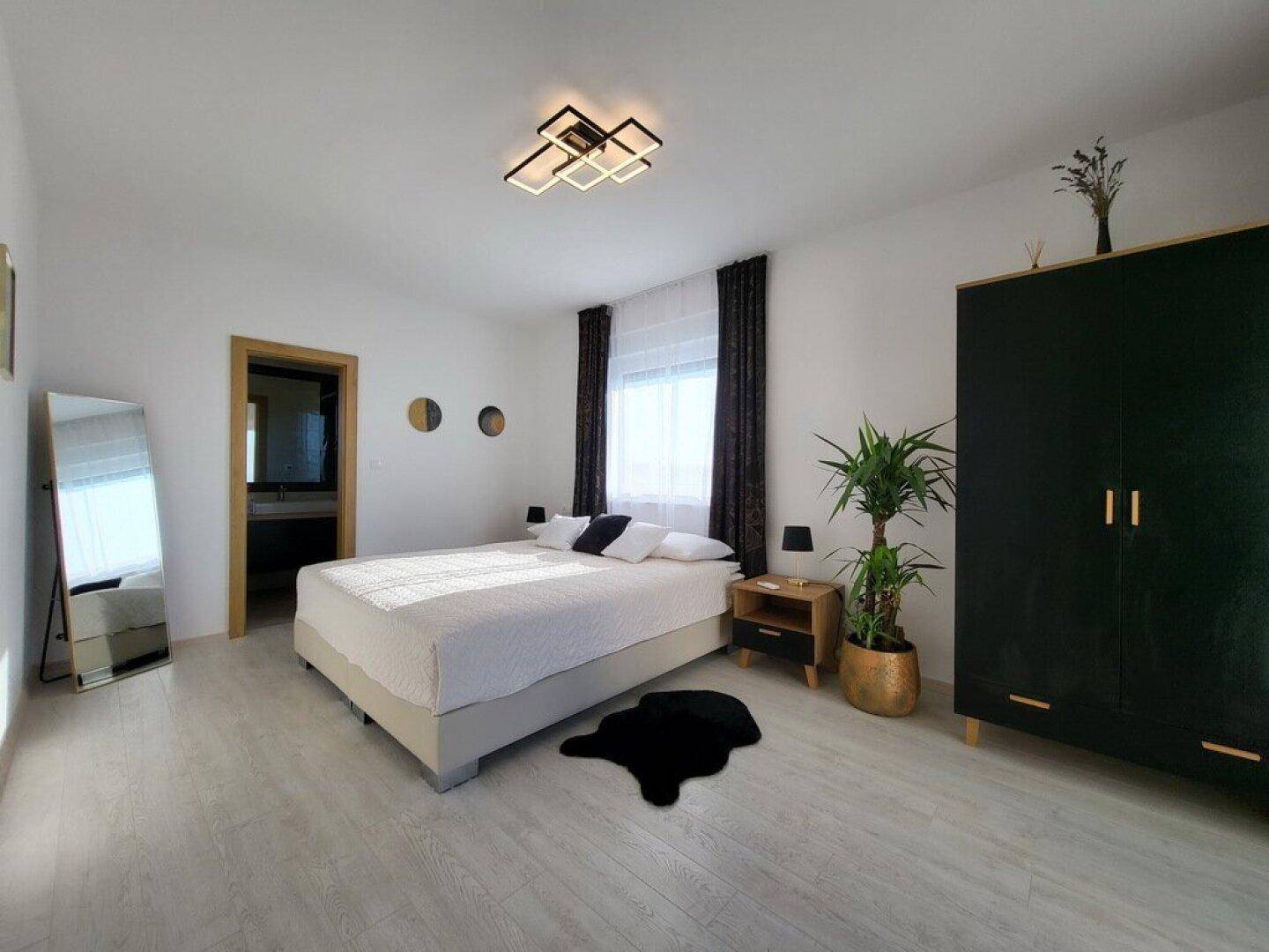 Modernes Schlafzimmer mit dunklem Kleiderschrank, Spiegel und hellem Holzboden.