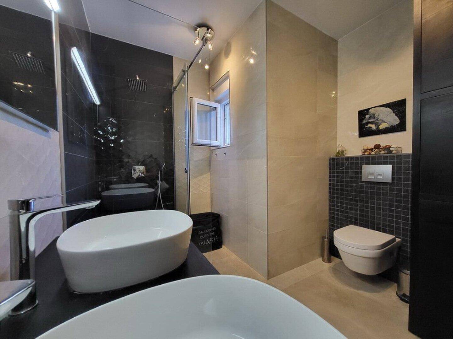 Stilvolles Badezimmer mit Doppelwaschbecken, wandhängendem WC und begehbarer Dusche.