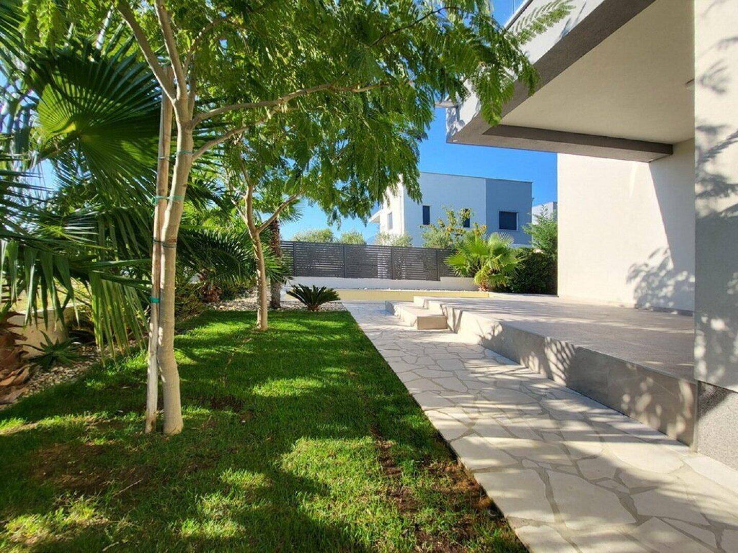 Gepflegter Gartenbereich mit Rasen, jungen Bäumen und Steinplattenweg neben dem Haus.