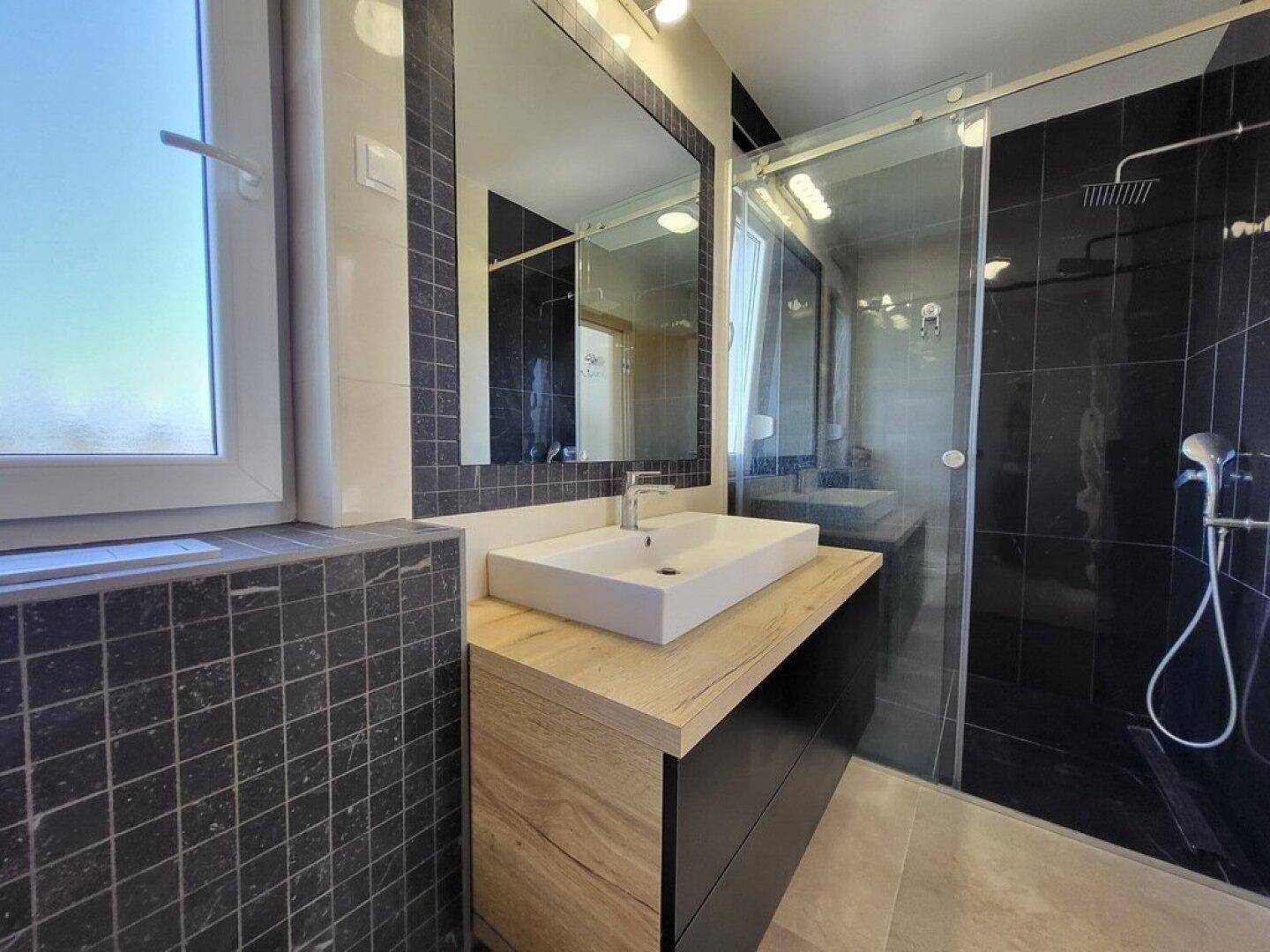 Modernes Badezimmer mit Einzelwaschbecken, Duschkabine und Fenster für Tageslicht.