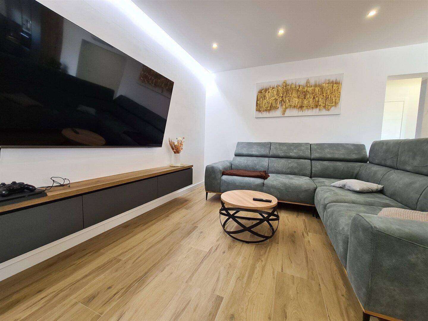 Geräumiges Wohnzimmer mit modernen Möbeln, Holzboden und indirekter Beleuchtung.