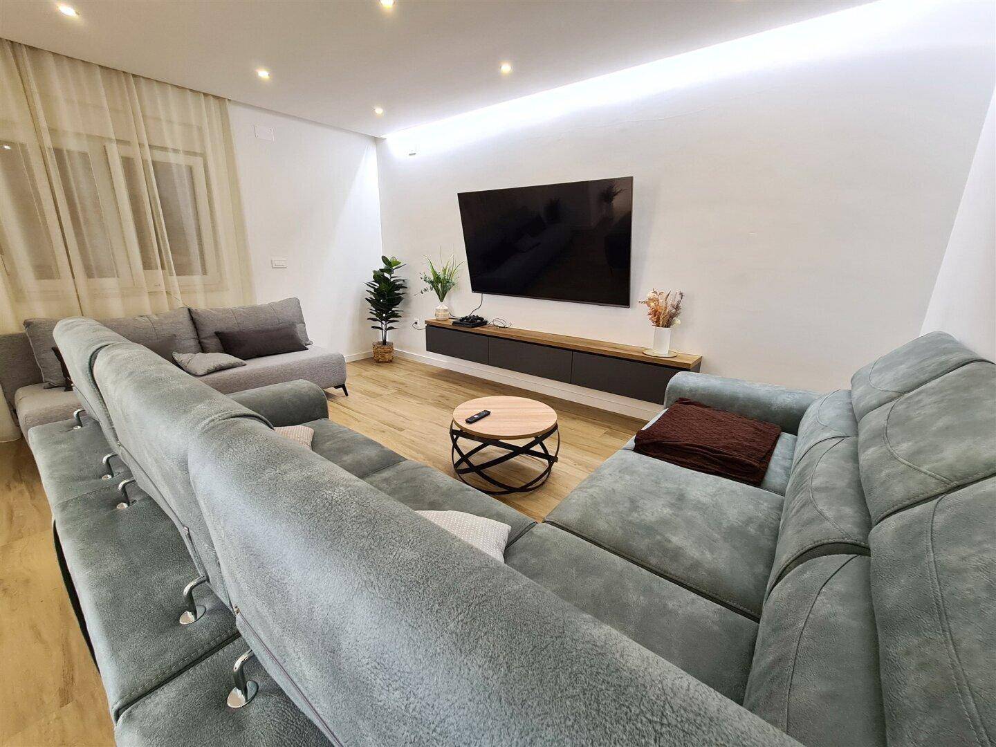 Helles Wohnzimmer mit modernen Sofas, großem Fernseher und indirekter Beleuchtung.