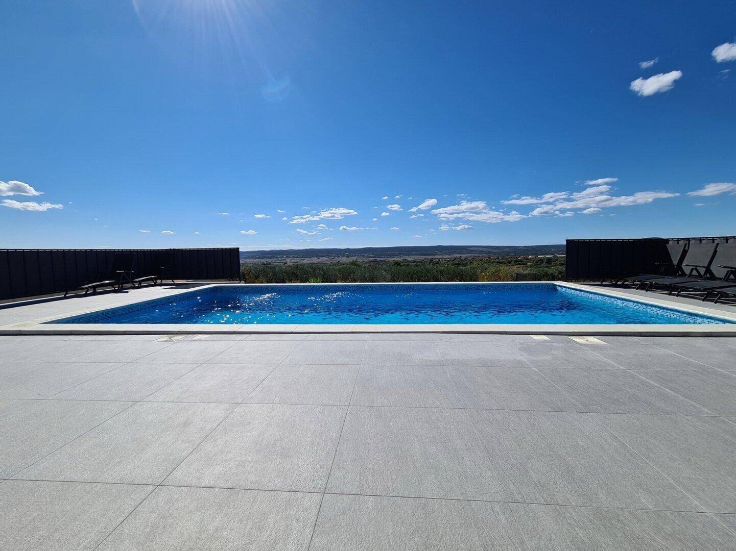 Großer Swimmingpool mit Liegeflächen und weitem Blick über die grüne Landschaft.