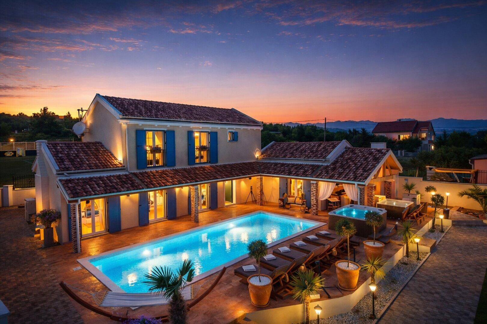 Exklusives Anwesen mit großem Pool, Whirlpool und gemütlicher Außenlounge, stimmungsvoll beleuchtet bei Sonnenuntergang.