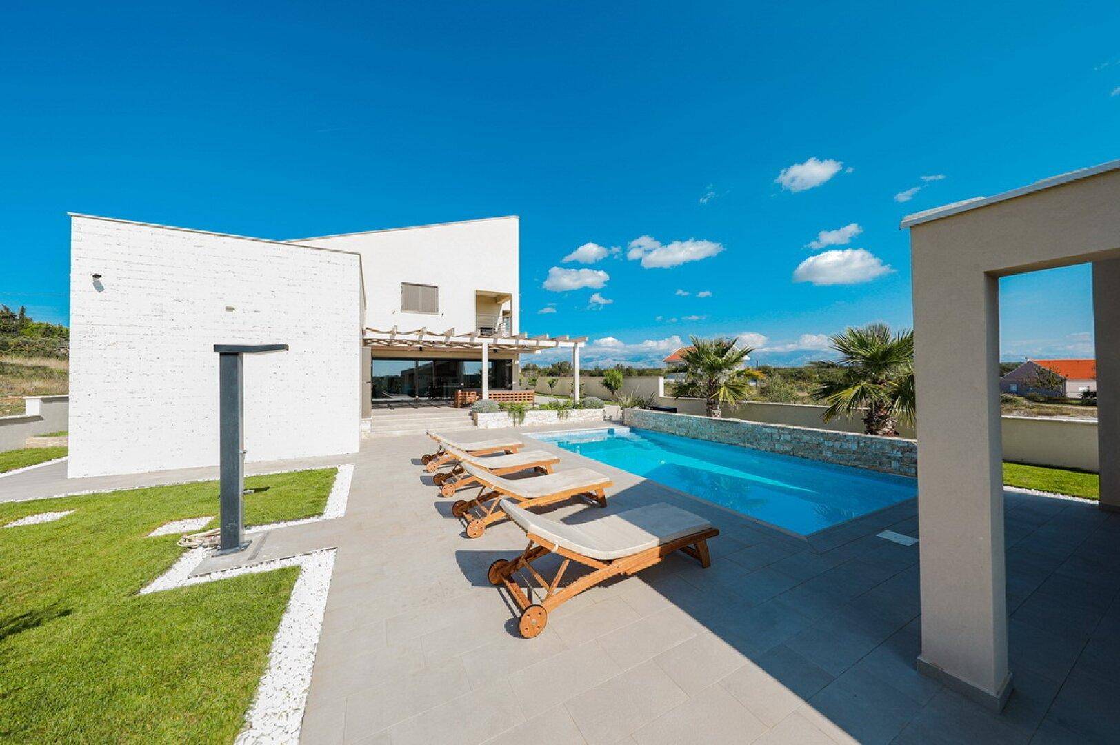 Weitläufiger Außenbereich mit Pool, Sonnenliegen und moderner Architektur der Villa.