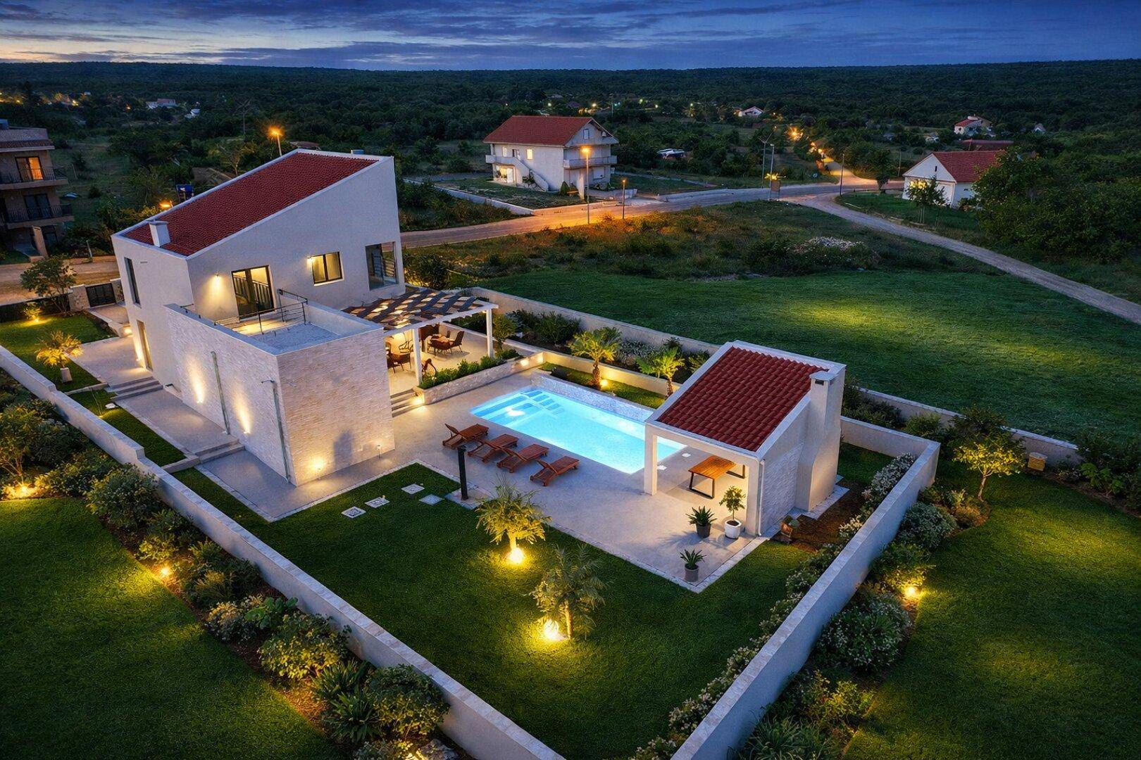 Luxuriöse Villa mit beleuchtetem Pool und Gartenanlage bei Sonnenuntergang, umgeben von Natur.