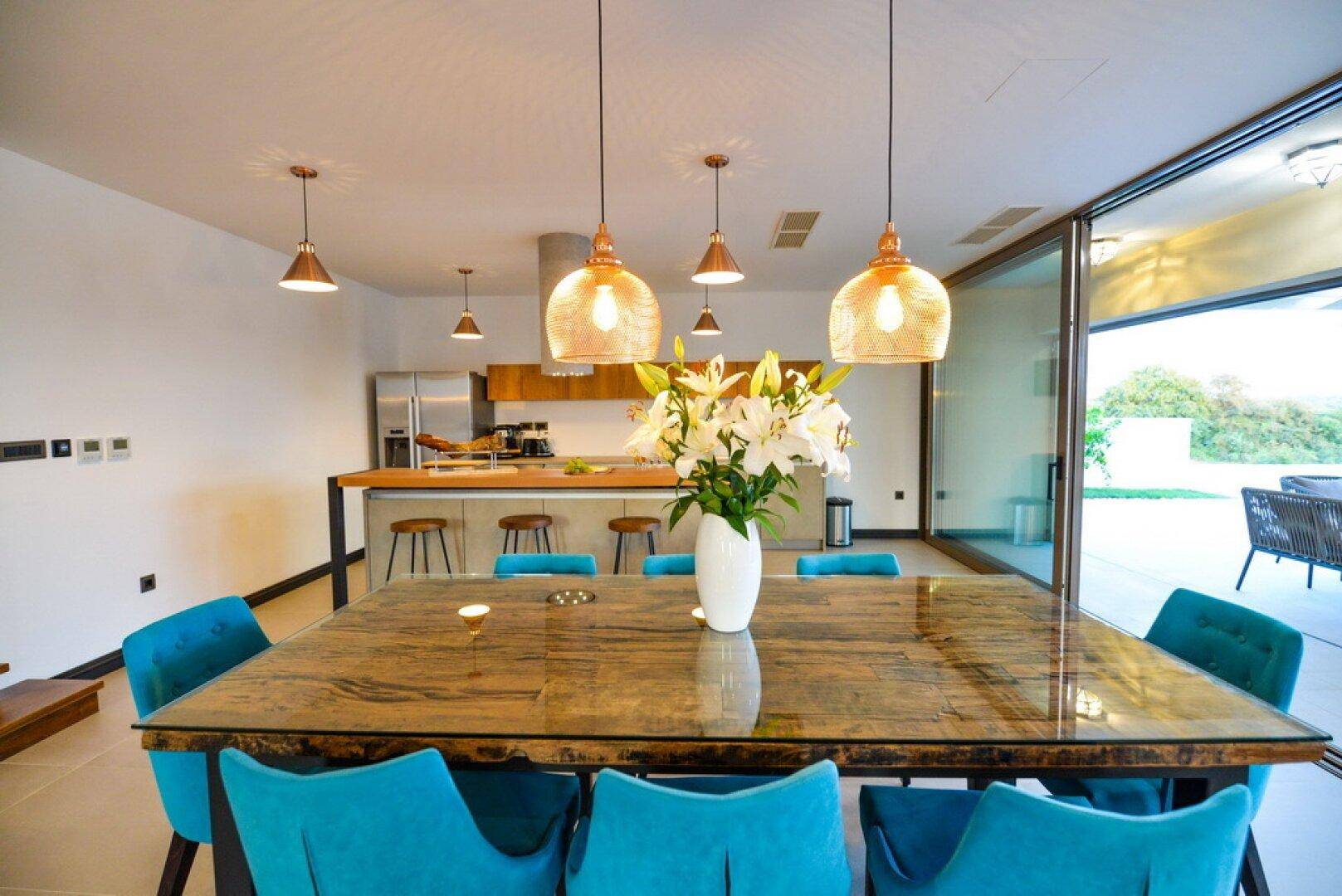Moderner Essbereich mit Holztisch, blauen Stühlen und offener Küche im Hintergrund.