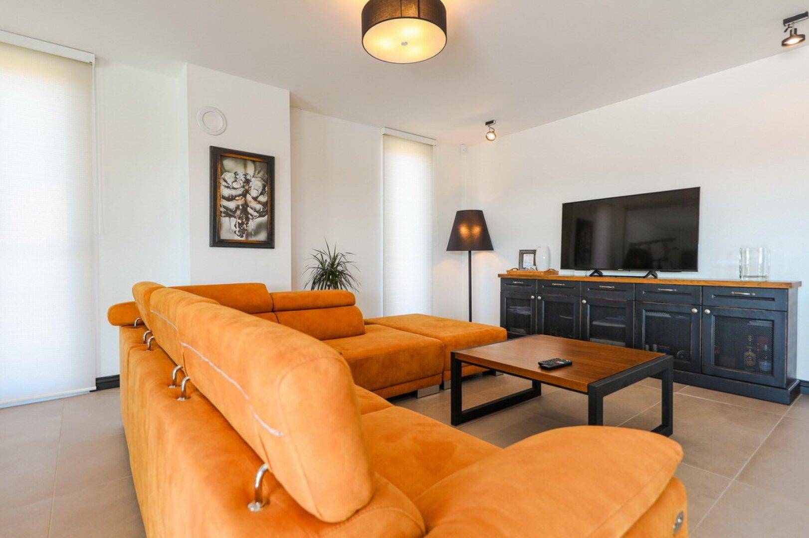Heller Wohnbereich mit großem orangefarbenem Ecksofa und modernem TV-Möbel.