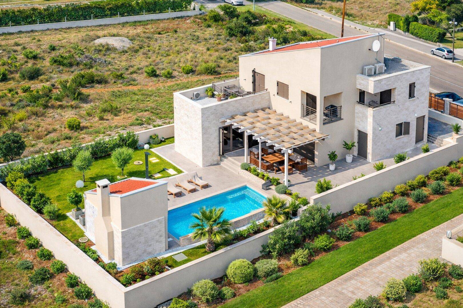 Vogelperspektive der modernen Villa mit Pool, Garten und umliegender Landschaft unter blauem Himmel.