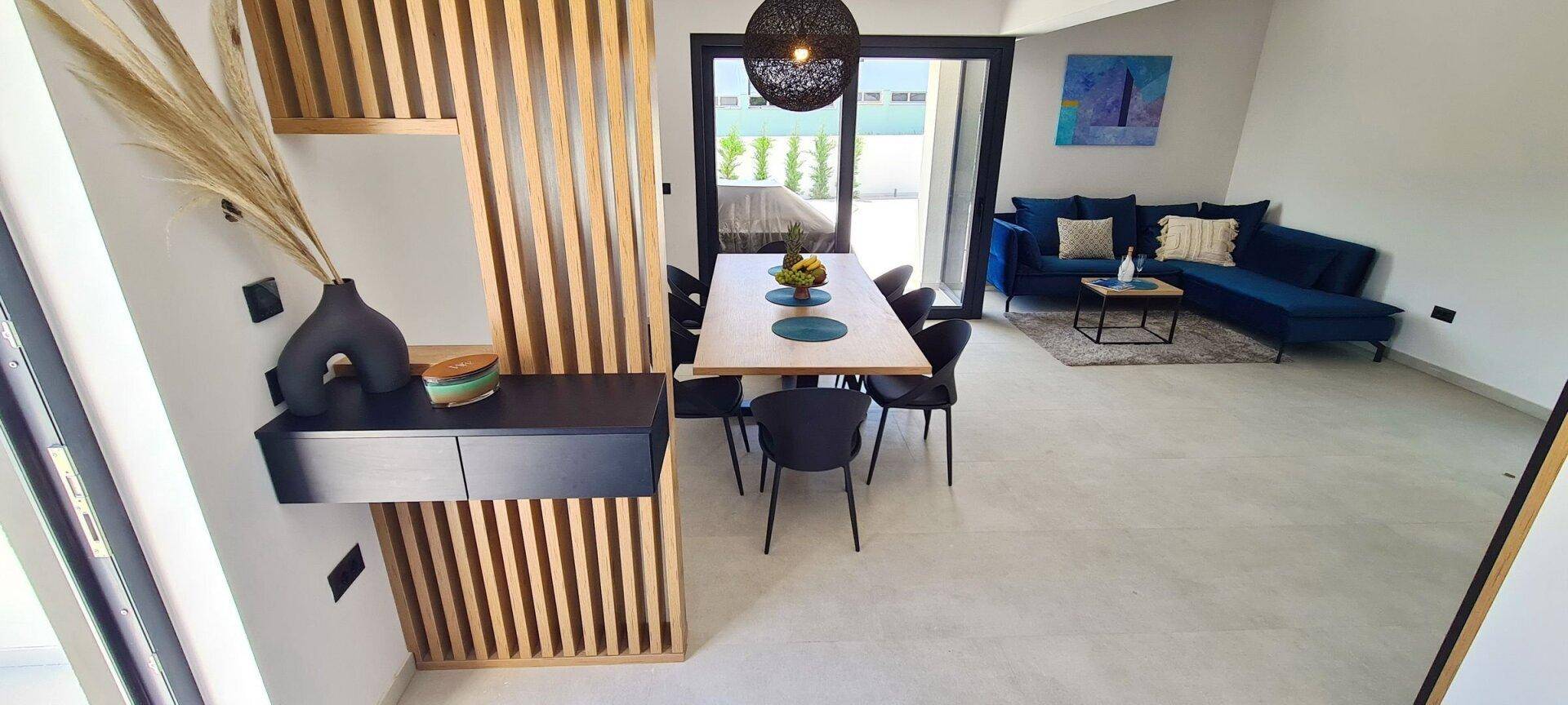 Offener Wohn- und Essbereich mit modernem Design, blauen Sofas und Zugang zur Terrasse.