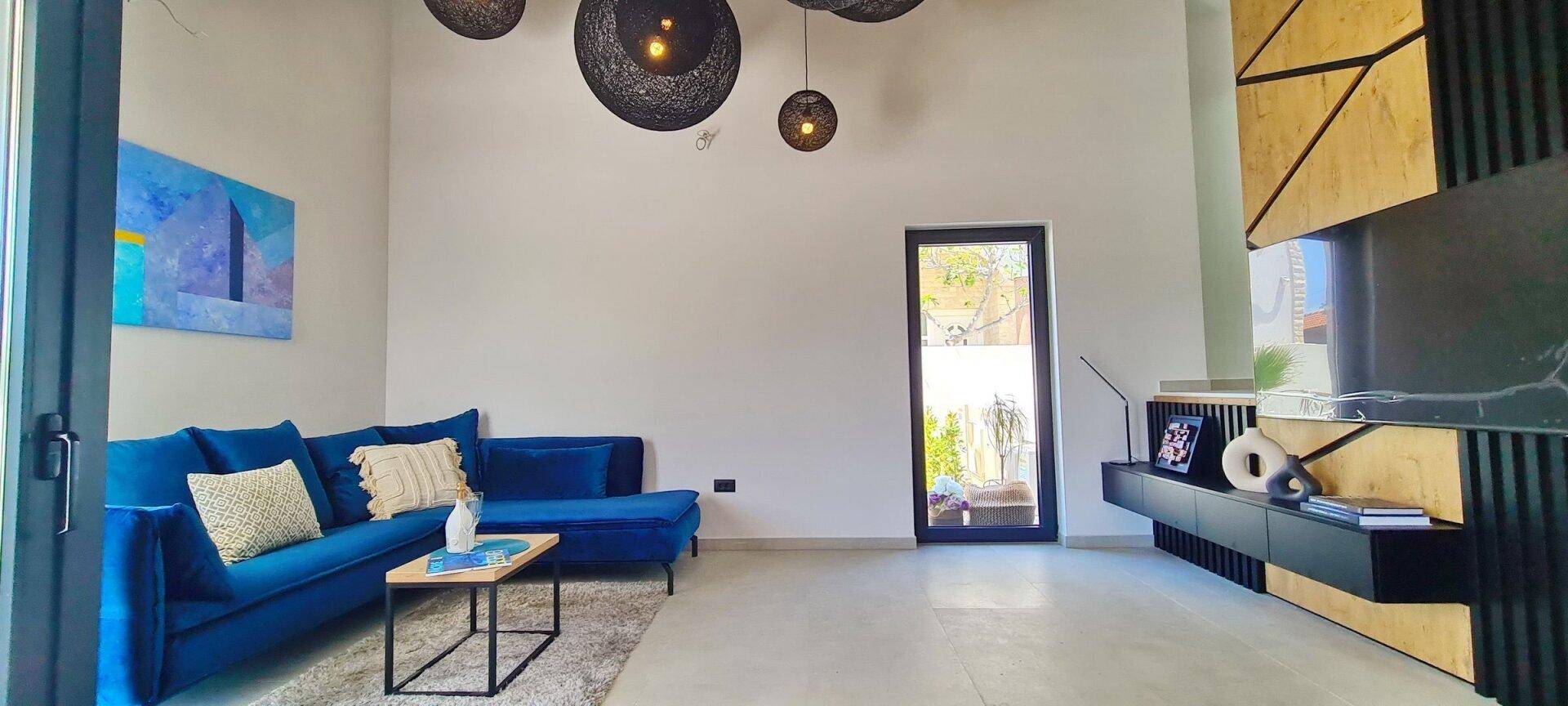 Helles Wohnzimmer mit bequemen blauen Sofas, modernen Leuchten und Zugang zum Außenbereich.