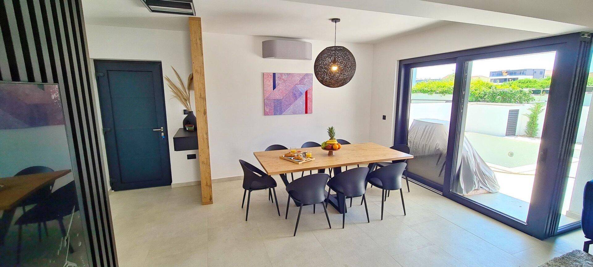 Heller Essbereich mit großem Holztisch, modernen Stühlen und Schiebetüren zur Terrasse.