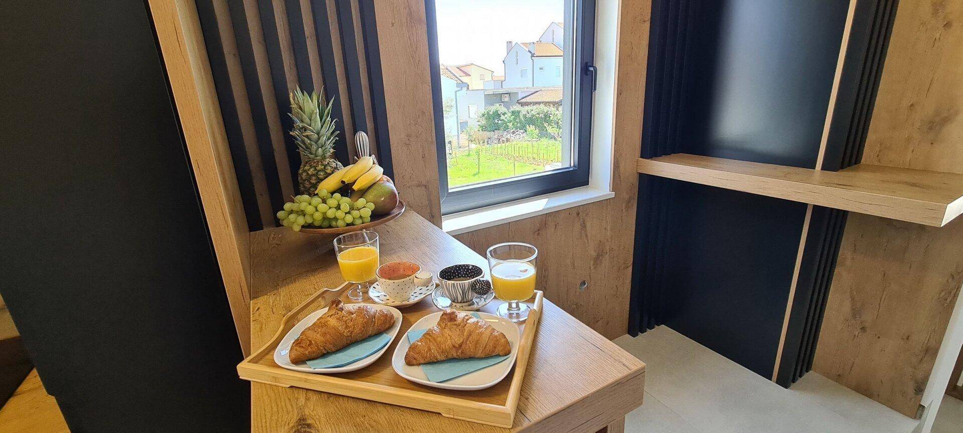 Gemütlicher Frühstücksbereich mit frischem Obst und Gebäck am Fenster mit Blick ins Grüne.