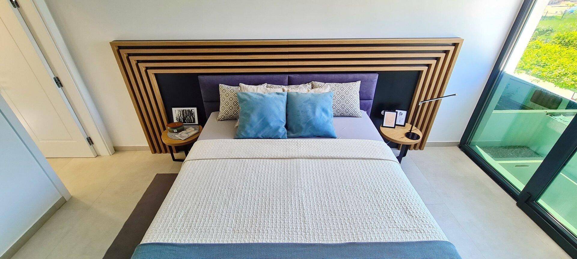 Modernes Schlafzimmer mit großem Bett, Holzkopfteil und bodentiefen Fenstern für viel Licht.
