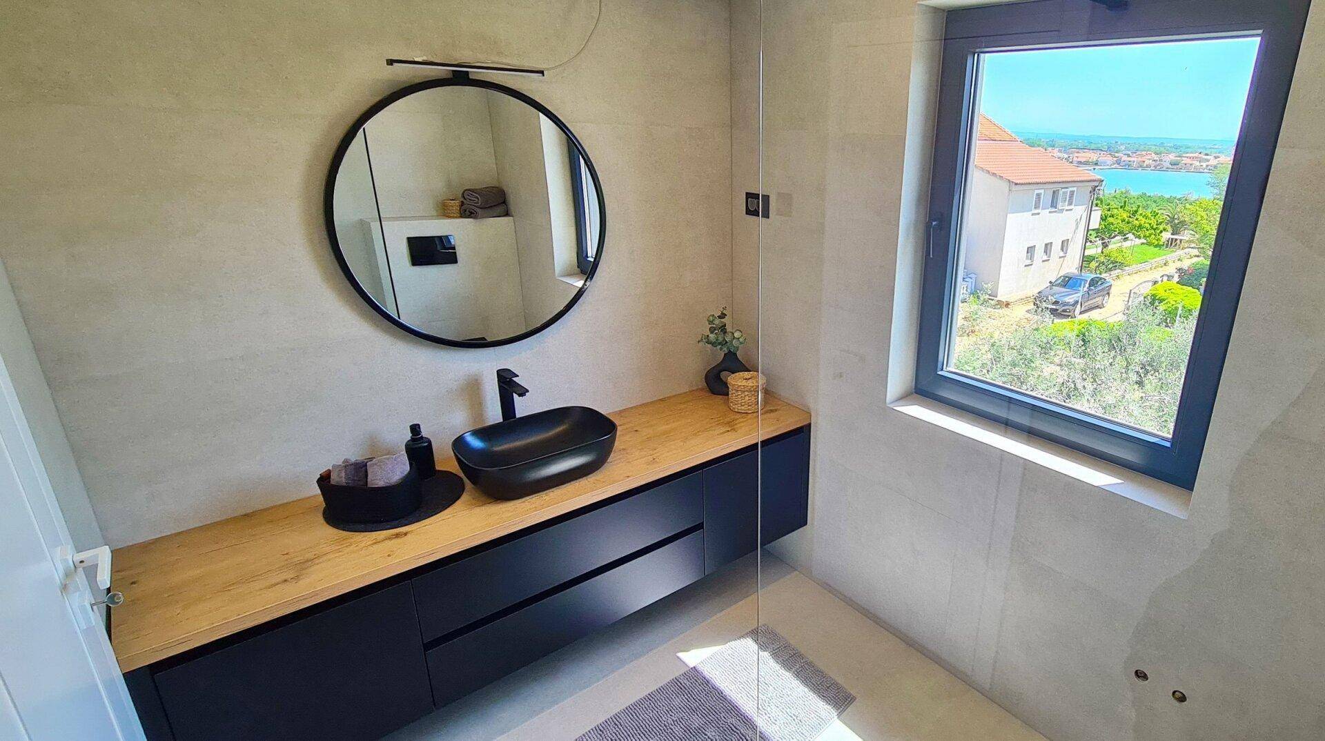 Modernes Badezimmer mit großem Fenster, schwarzem Waschbecken und begehbarer Dusche.