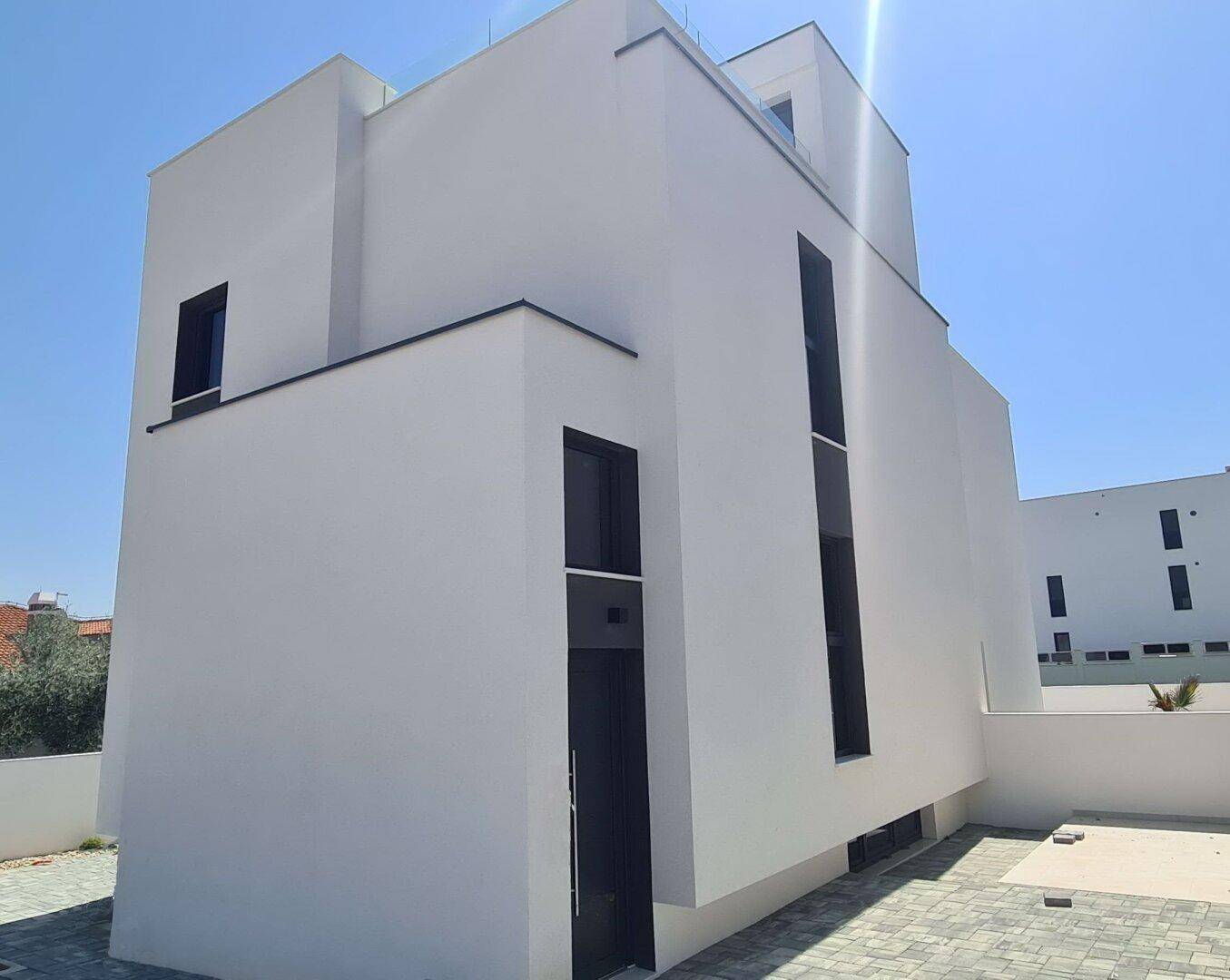 Zeitgenössische weiße Villa mit minimalistischem Design und großen Fenstern unter blauem Himmel.