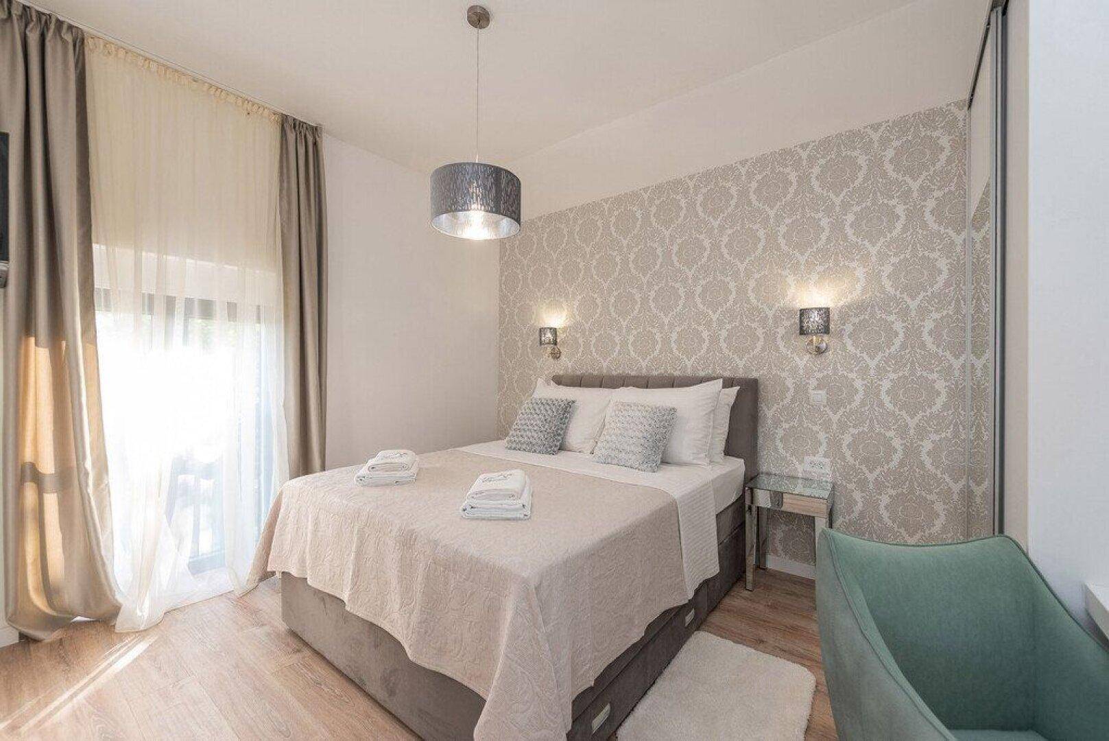 Gemütliches Schlafzimmer mit Doppelbett, gemusterter Tapete und Balkonzugang.