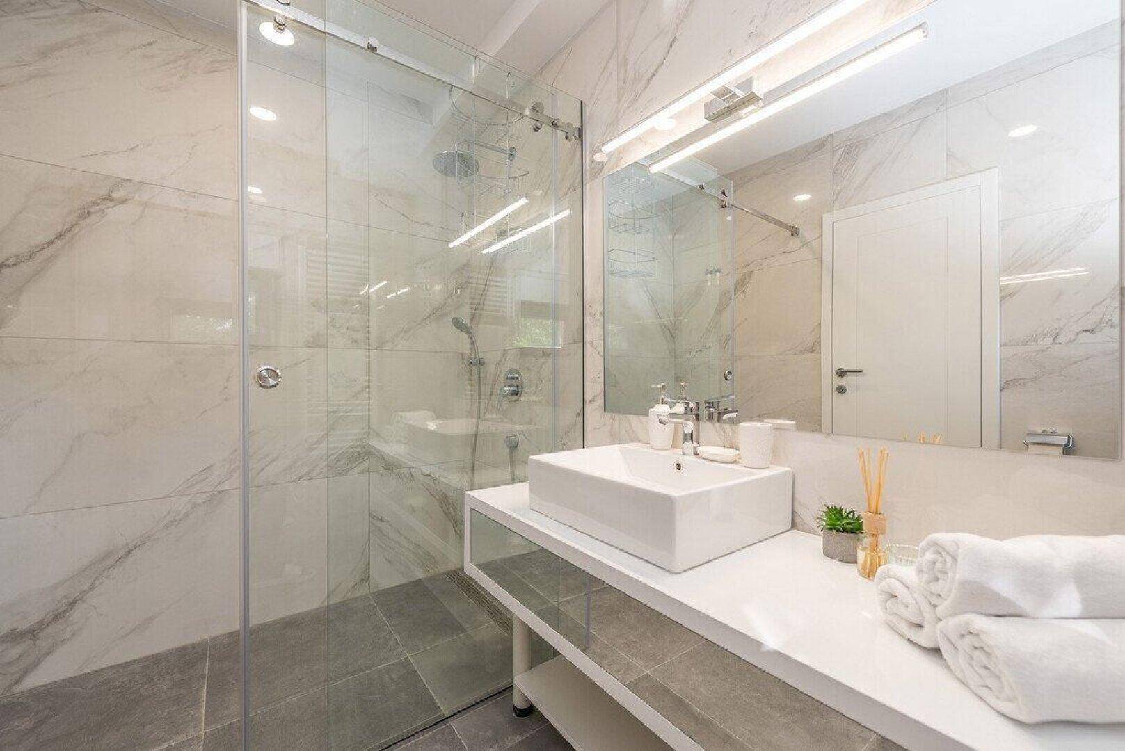 Modernes Badezimmer mit begehbarer Dusche, Marmorfliesen und elegantem Waschbecken.