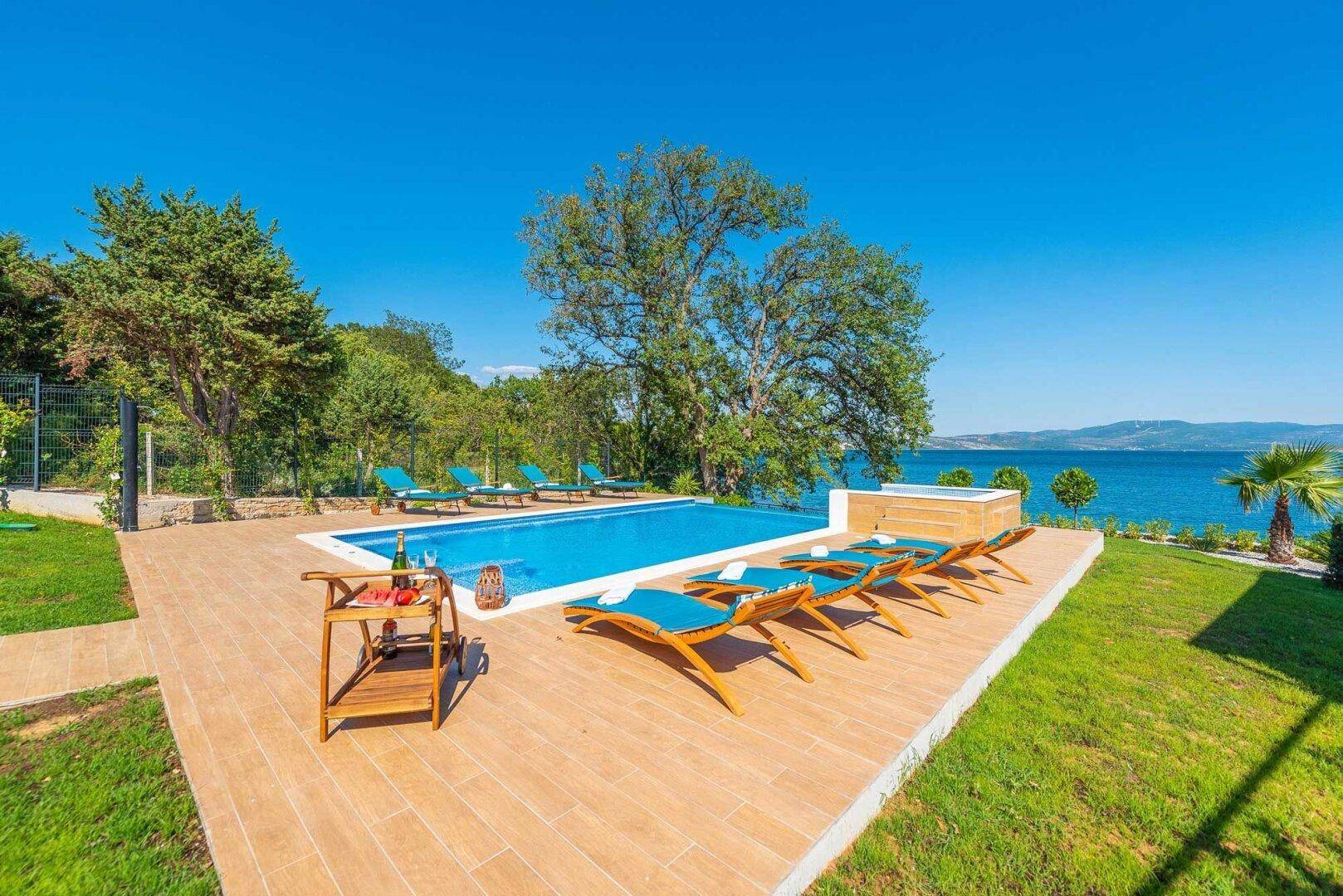Weitläufiger Poolbereich mit Liegestühlen, Rasenfläche und Meerblick.