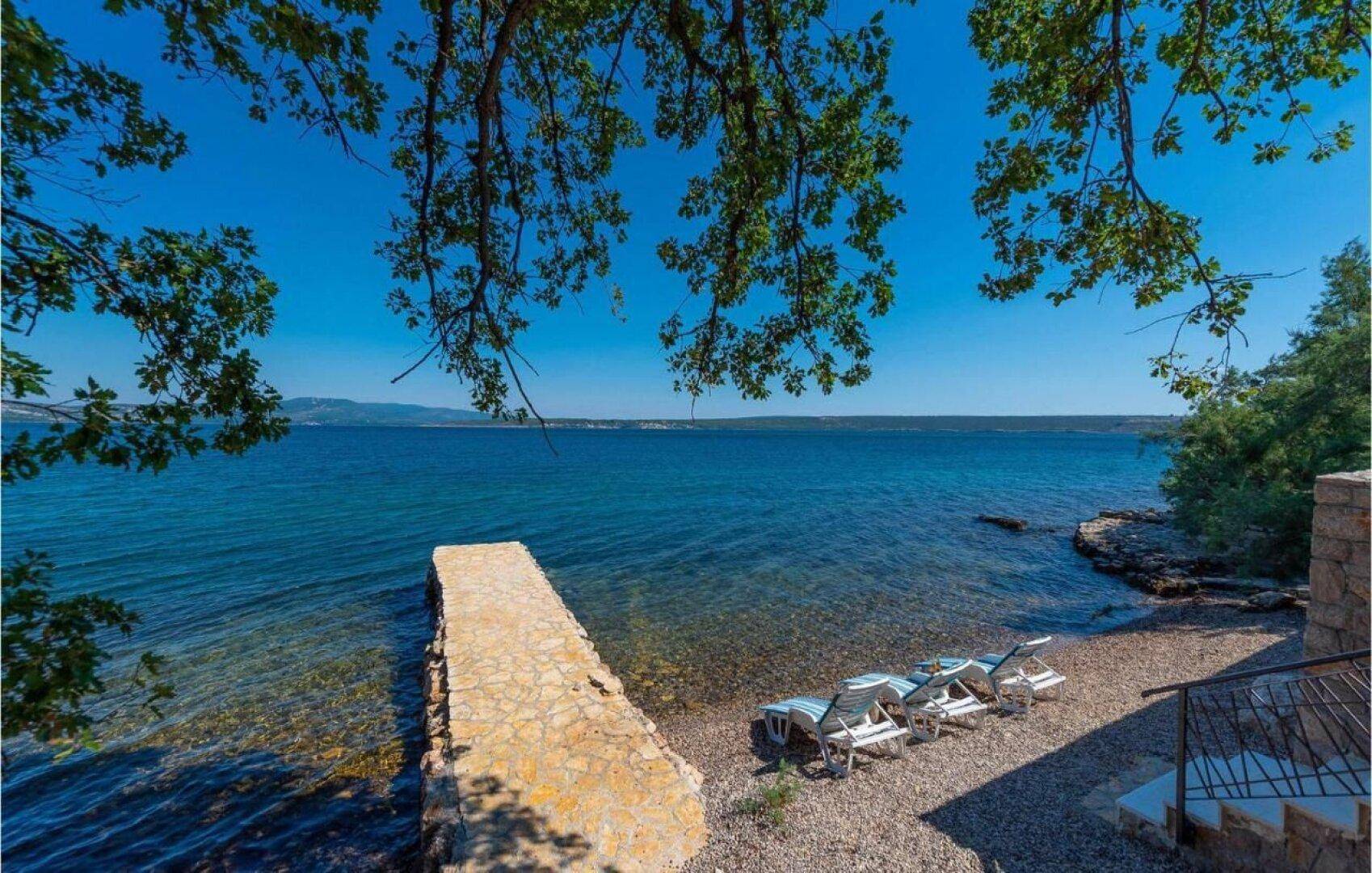 Privater Zugang zum Meer mit Steinpier und Liegestühlen am Kieselstrand.