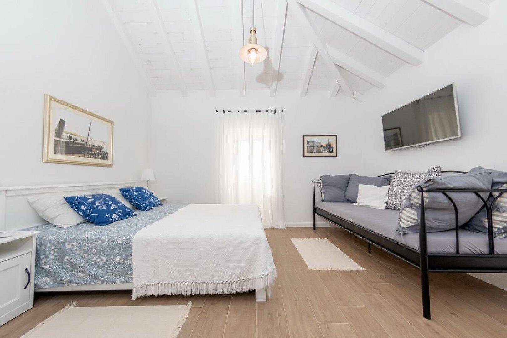 Helles Schlafzimmer mit Holzbalkendecke, Doppelbett und Tagesliege.