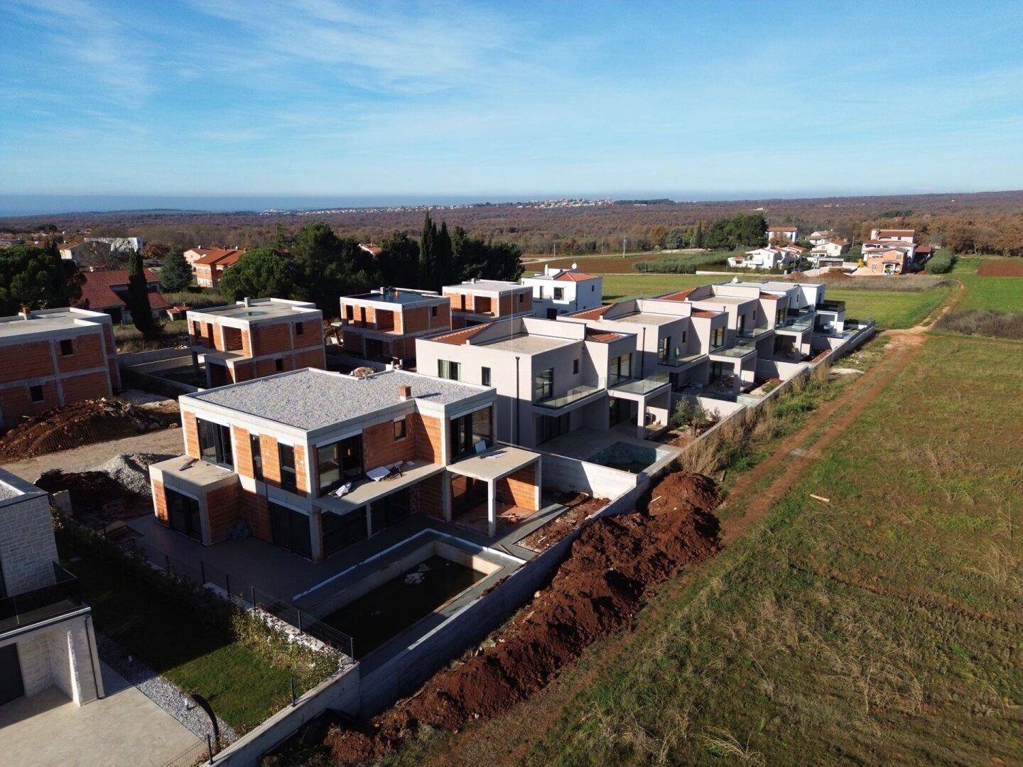 Luftaufnahme einer modernen Wohnsiedlung mit Neubauten und im Bau befindlichen Häusern in ländlicher Umgebung.