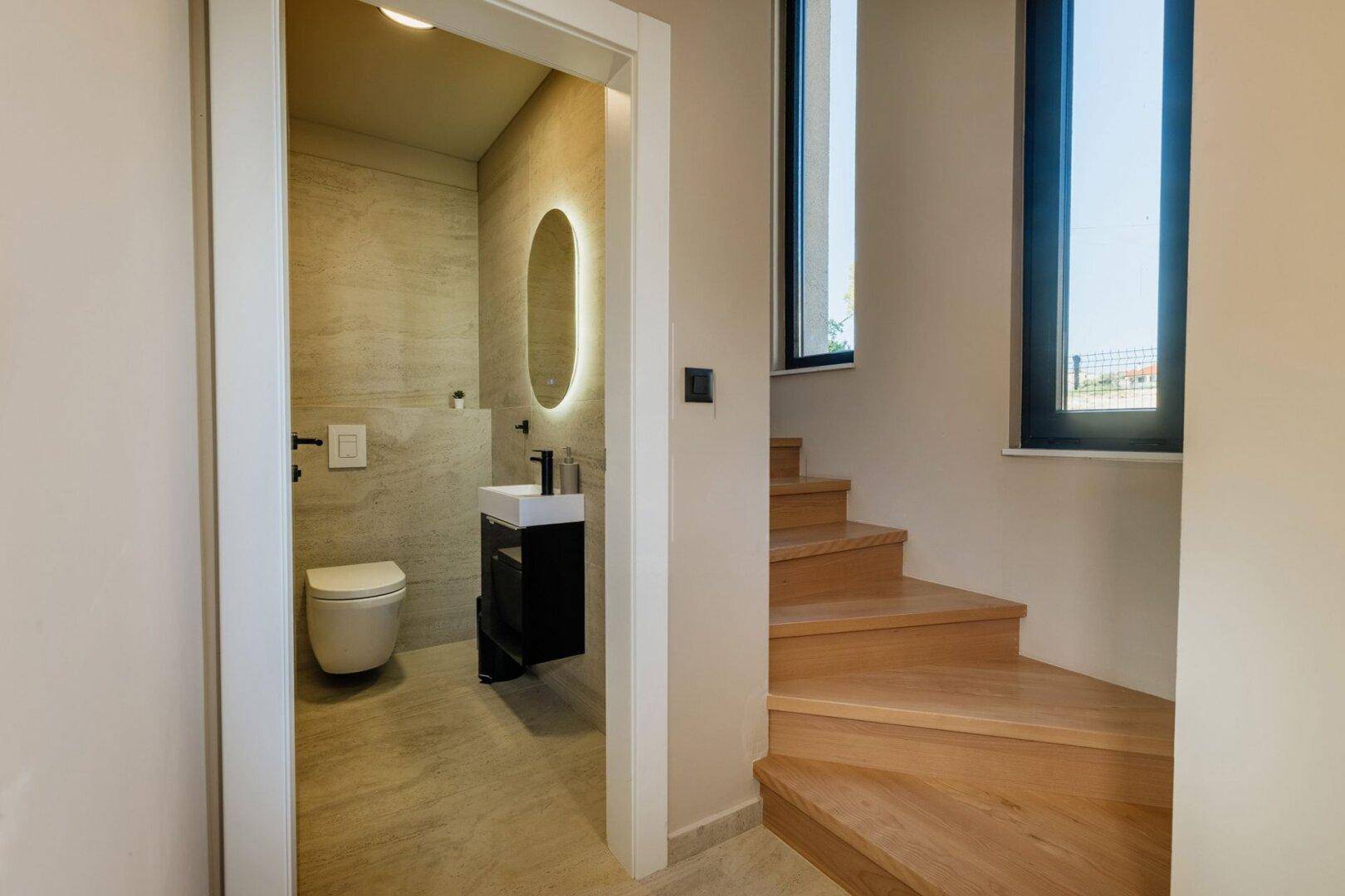 Elegantes Gäste-WC mit modernem Design, Wand-WC und beleuchtetem ovalen Spiegel.