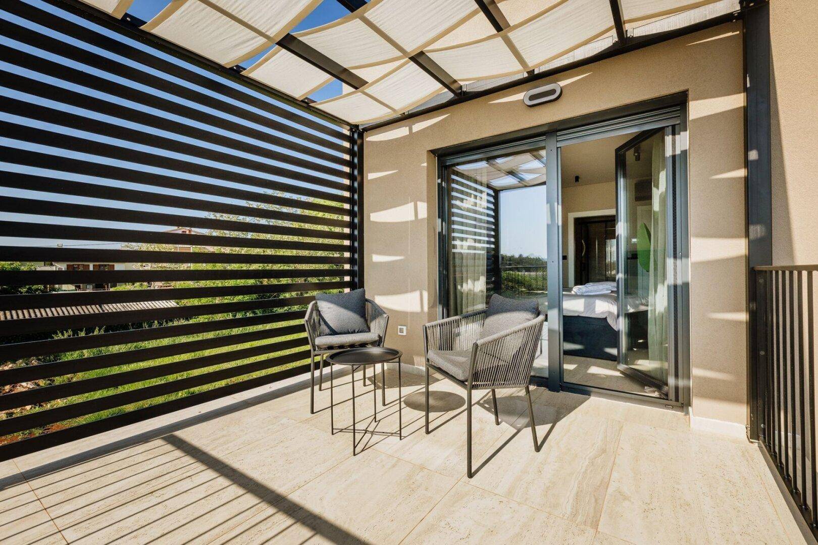 Überdachter Balkon mit modernen Sitzmöbeln und Blick ins Grüne.