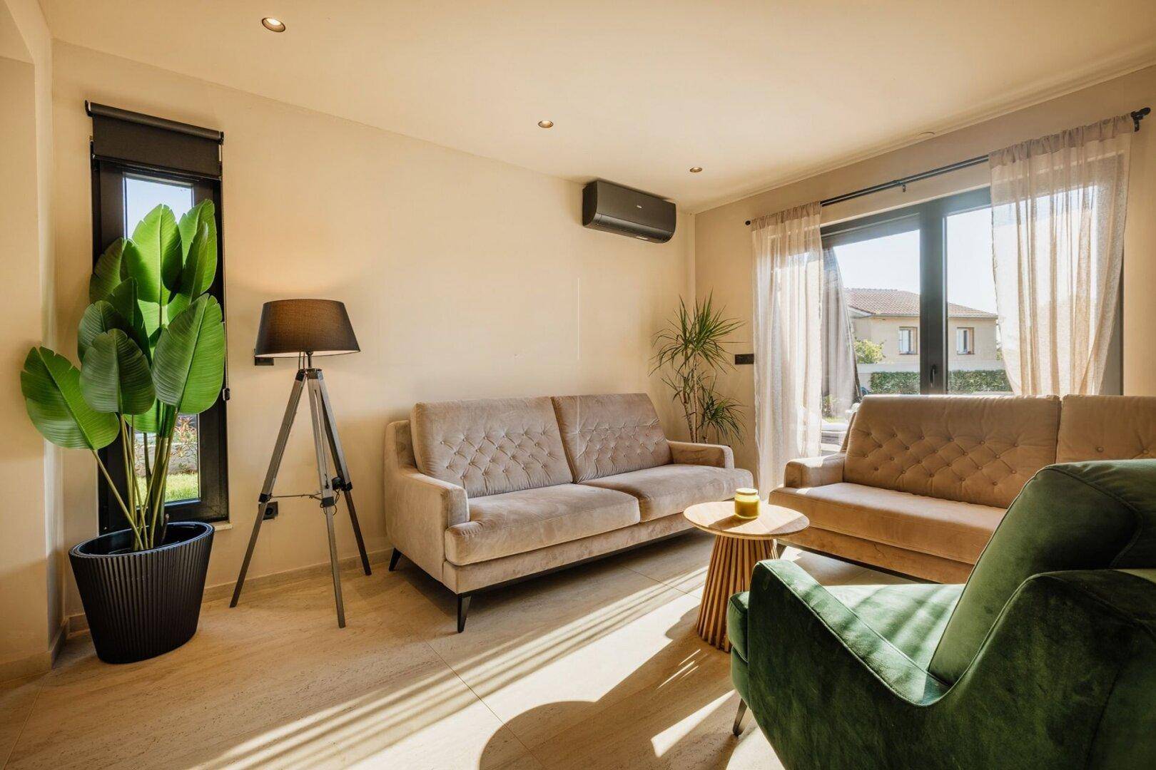 Gemütliches Wohnzimmer mit beigen Sofas, grüner Akzentfarbe und Klimaanlage.