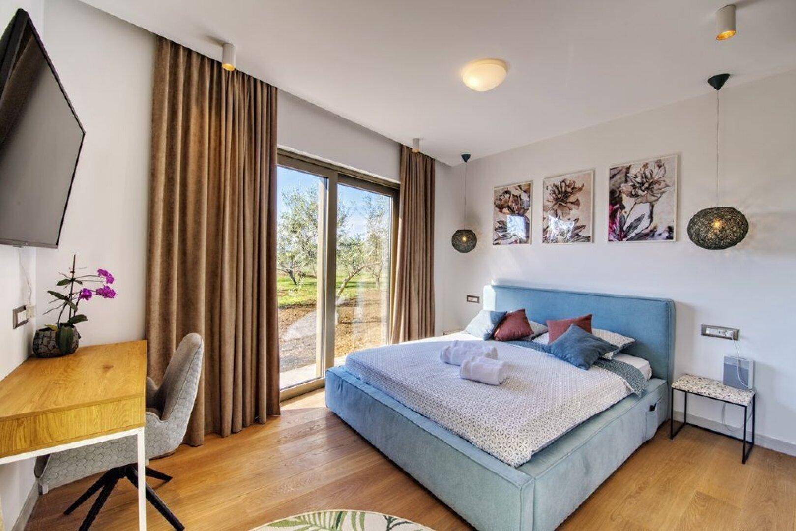 Helles Schlafzimmer mit großem Bett, Holzboden und direktem Zugang zum Garten.