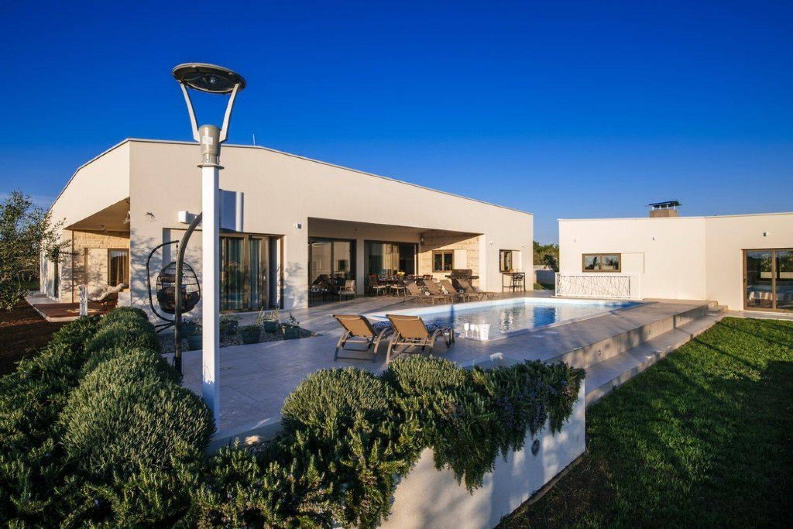 Moderne Villa mit Swimmingpool, gepflegtem Garten und klarem blauen Himmel.