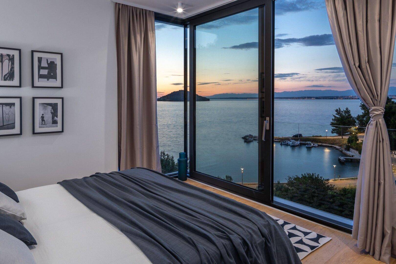 Schlafzimmer mit atemberaubendem Meerblick bei Sonnenuntergang durch große Fenster.