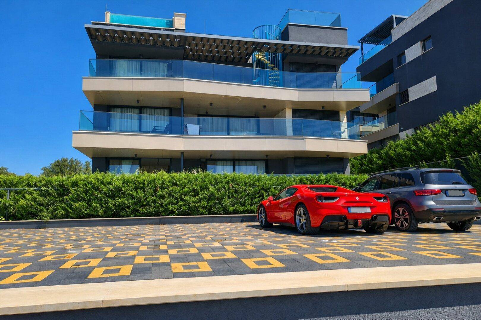 Modernes Apartmentgebäude mit mehreren Balkonen, Glasfassade und gepflegtem Parkplatzbereich.