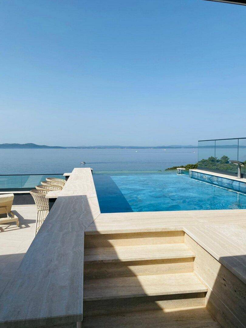 Einladender Infinity-Pool mit weitem Meerblick und sonnigen Stufen, die zum Wasser führen.